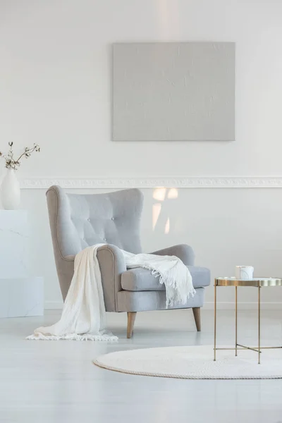 White blanket on grey armchair next to coffee table in bright living room