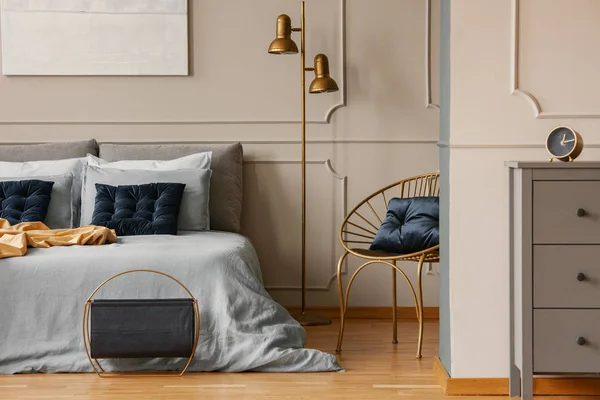青い寝具とダークブルーの枕を備えたキングサイズベッドの隣のスタイリッシュな金色のランプ — ストック写真