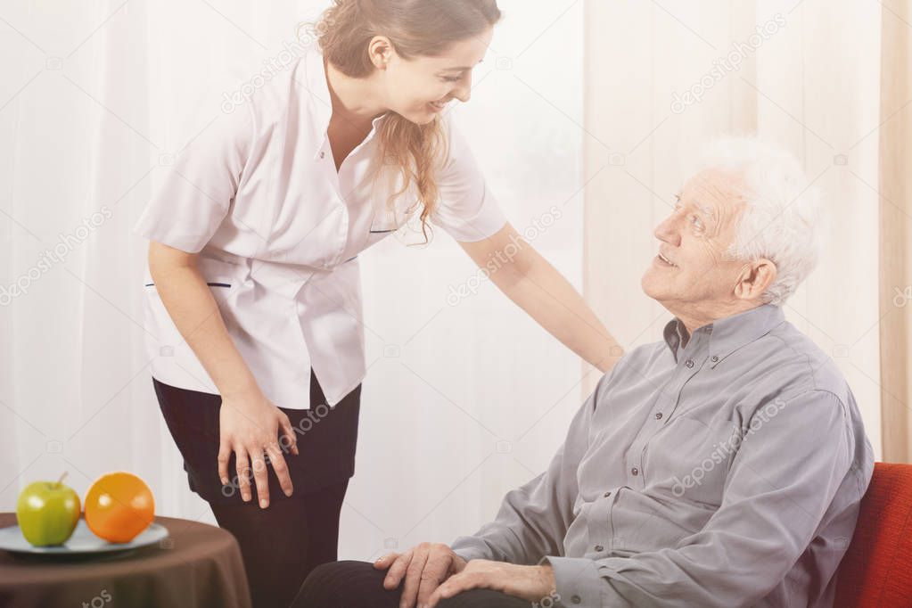 Old man in nursing home with helpful carer at his side