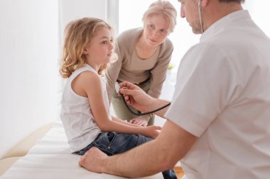 Pnömoni ile sevimli çocuk muayene Pediatrist, arkalarında endişeli anne