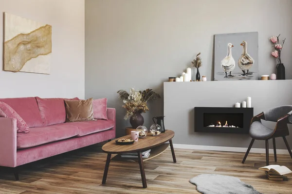 Dry flowers in pottery vase on small wooden table next to velvet pink couch in grey living room — Stock Photo, Image