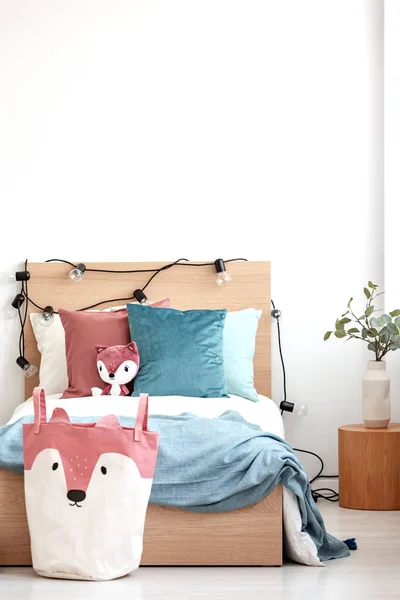 Cuscini in velluto rosa pastello e turchese e volpe giocattolo su letto singolo in legno con lenzuola e coperte bianche — Foto Stock