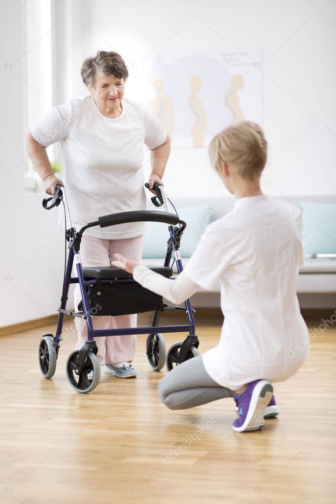 Senior woman with walker trying to walk again and helpful physiotherapist supporting her