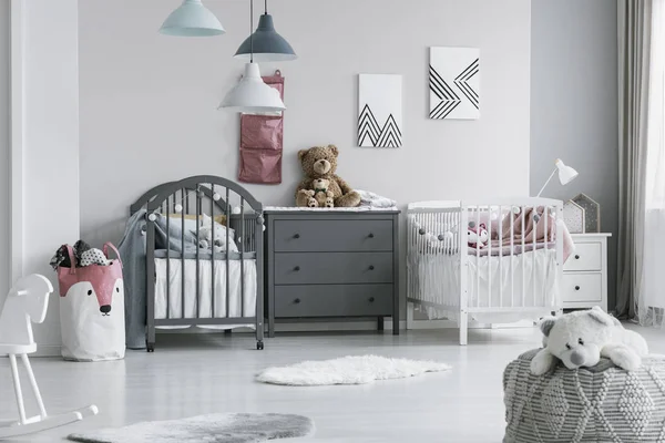 Brown teddy bear on grey wooden commode between two cribs in fashionable bedroom for twins — Stock Photo, Image