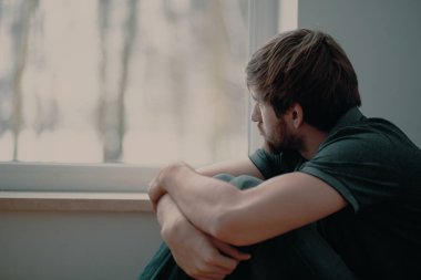 Üzgün genç adam pencereden bakarak katta oturan