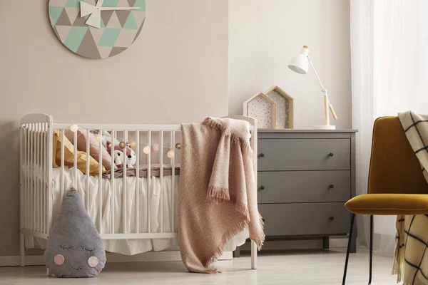 Подушки и игрушки в белой деревянной кроватке с пастельно-розовым одеялом в яркой детской — стоковое фото