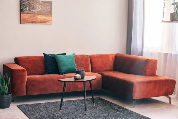 Elegante pequena mesa de café de madeira com abaixa na frente de grande sofá de canto de veludo com travesseiros — Fotografia de Stock