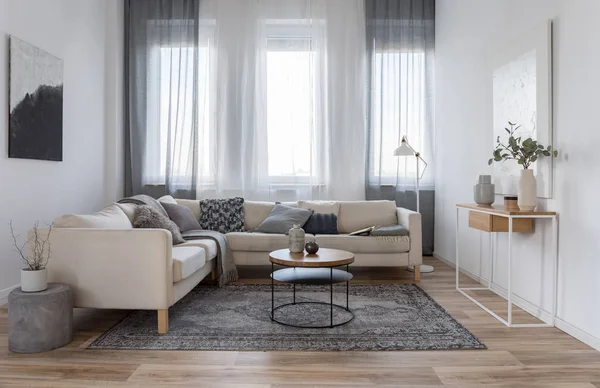 Beżowy wygodna sofa narożna z szarymi poduszkami w eleganckim wnętrzu salonu z białą ścianą — Zdjęcie stockowe