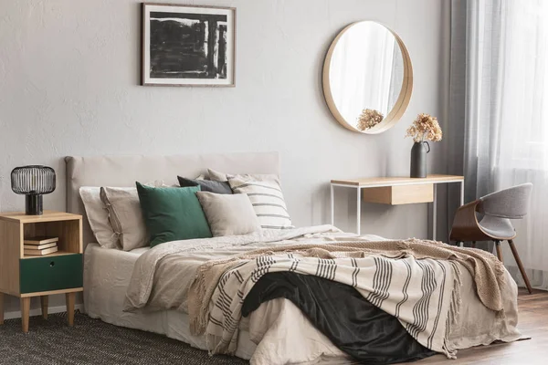 Elegant round mirror in wooden frame above fancy console table with flowers in vase in trendy bedroom interior with beige vase — Stock Photo, Image