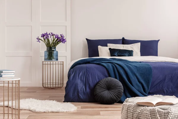ネイビーブルーの寝具付きキングサイズベッドの隣のベッドサイドテーブルの花瓶の花 — ストック写真
