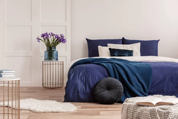 Bloemen in vaas op nachtkastje naast King size bed met marineblauw beddengoed — Stockfoto