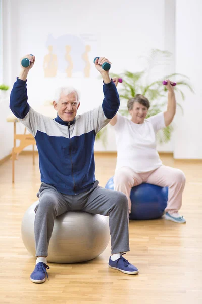 Hombre y mujer mayores haciendo ejercicio en las bolas de gimnasia durante la sesión de fisioterapia en el hospital —  Fotos de Stock