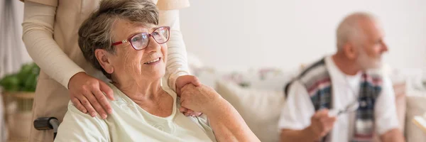 Vue panoramique de dame âgée en fauteuil roulant tenant la main avec le soutien bénévole debout derrière elle — Photo