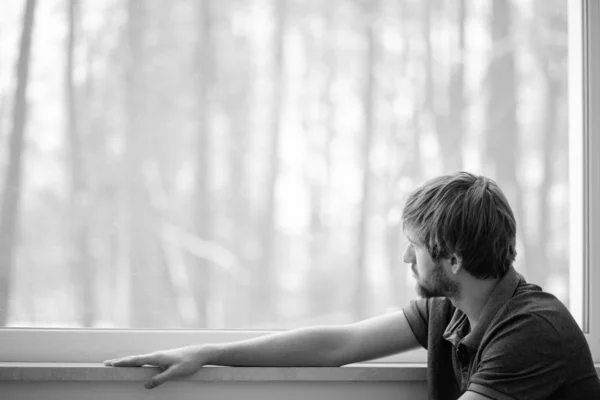 Молодой человек сидит на полу гостиной с большим окном — стоковое фото