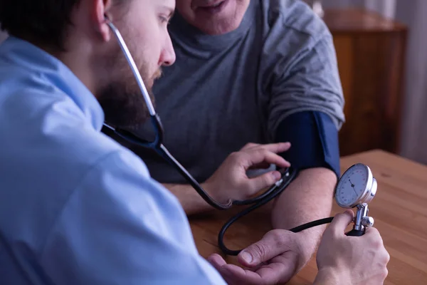 Primer plano de un joven enfermero midiendo la presión arterial del hombre mayor —  Fotos de Stock