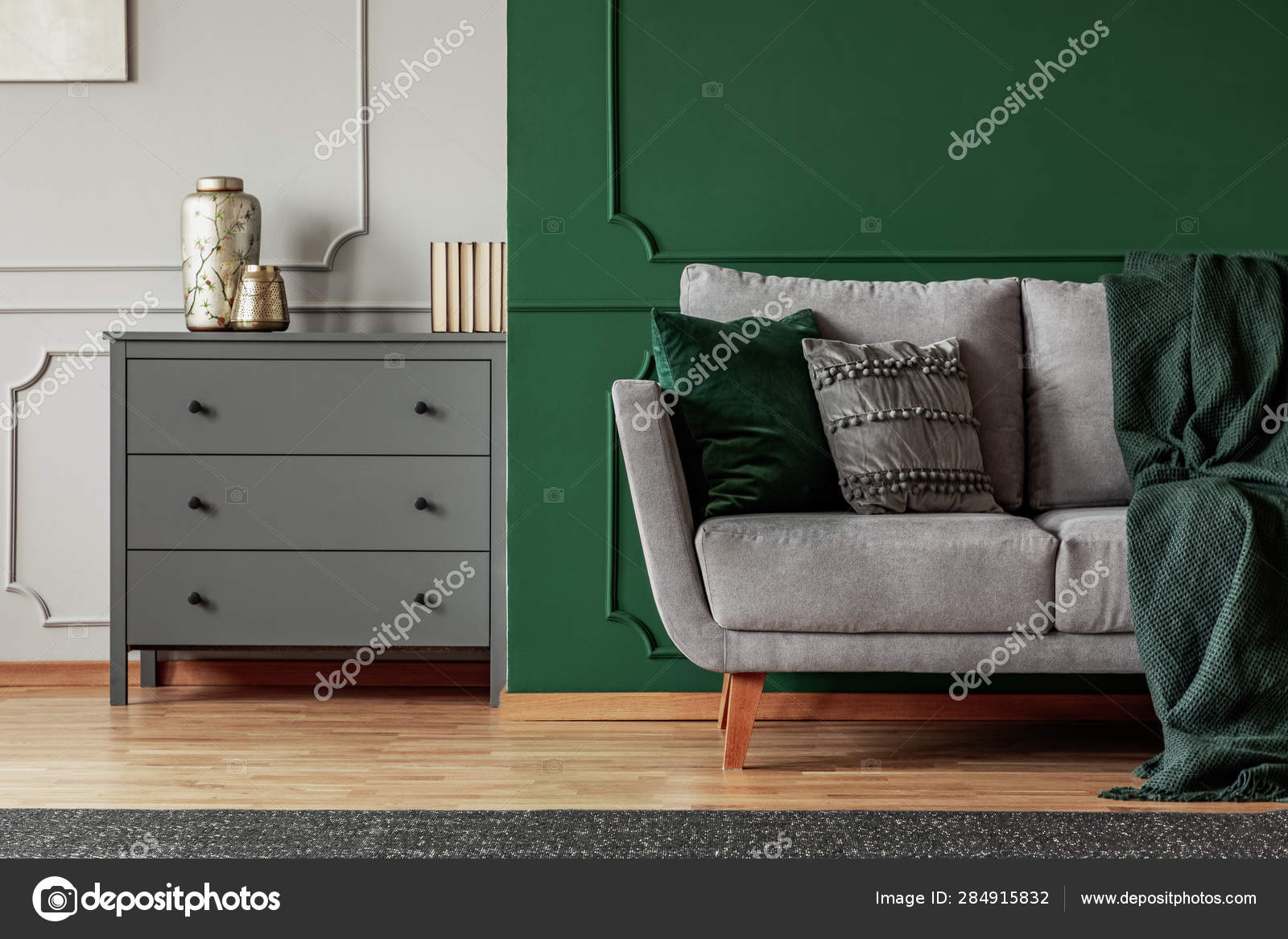 Green wall grey Scandinavian couch and wooden chest of drawers in