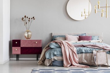 Mavi, pastel pembe ve bej yatak ve kadife kaplı komodiler ile sıcak yatak ile şık yatak odası iç gri duvar üzerinde klas yuvarlak ayna