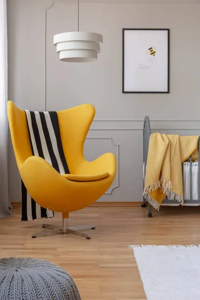 Svart och vitt täcke på gul Egg stol i grått babysovrum med grå spjälsäng med mysig filt och affisch på väggen — Stockfoto