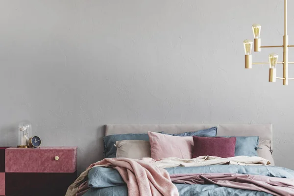 Veludo coberto pastel rosa e mesa de cabeceira borgonha ao lado da cama quente com cama azul e bege e travesseiros rosa — Fotografia de Stock