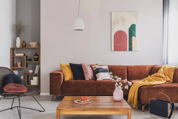 Flores em vaso na mesa de café de madeira na sala de estar elegante interior com sofá de canto marrom com travesseiros e pintura abstrata na parede — Fotografia de Stock