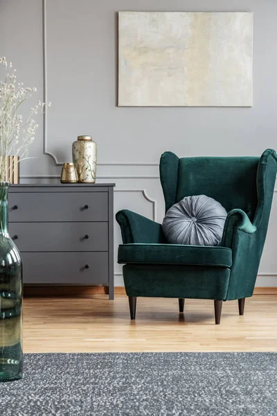 Poltrona verde esmeralda com travesseiro ao lado de commode de madeira cinza no interior da sala de estar escura — Fotografia de Stock