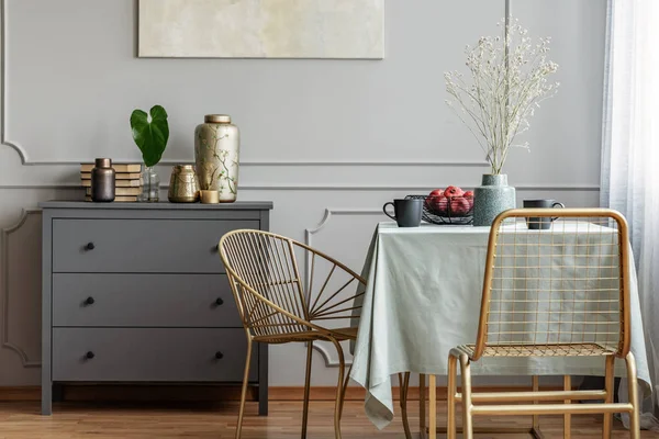 Interno della sala da pranzo con tavolo lungo, eleganti sedie dorate e comò in legno grigio — Foto Stock
