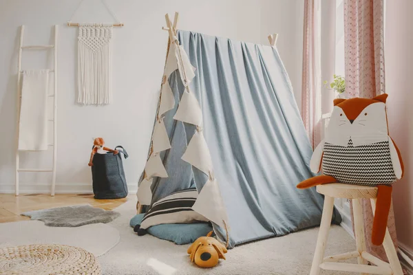 Natural playroom with blue scandinavian tent, wooden ladder, toys and handmade macrame on the wall, real photo