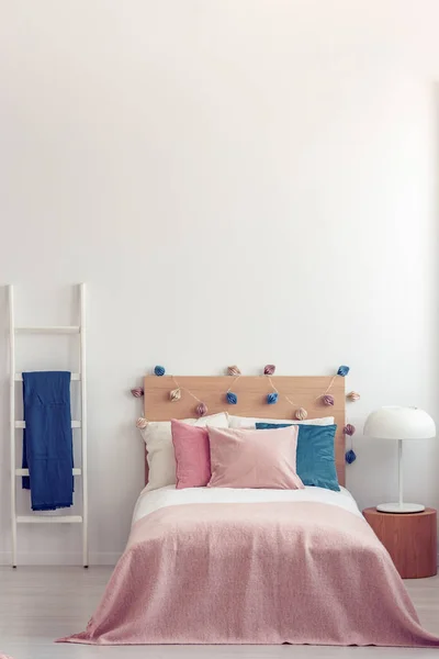 Almohada rosa pastel y manta en una cama de madera con ropa de cama blanca en el interior del dormitorio escandinavo —  Fotos de Stock