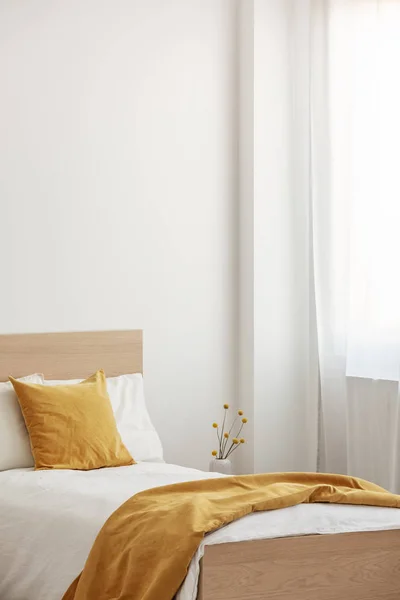 Primer plano de una sola cama de madera con ropa de cama blanca y amarilla, espacio para copiar en la pared vacía —  Fotos de Stock