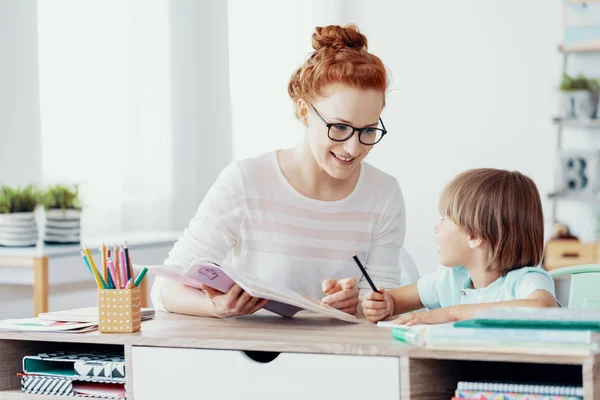 Mulher sorridente com livro ensinando menino durante aulas extra-curriculares — Fotografia de Stock
