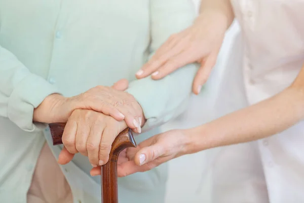 Close-up van oudere vrouw handen op houten Cane, behulpzame arts die haar steunt — Stockfoto