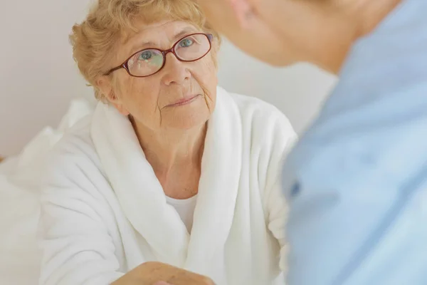 Traurige Seniorin mit Grippe schaut im Krankenhaus zu ihrem Arzt — Stockfoto