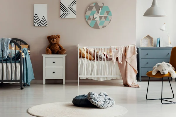 Foto real de dos almohadas sobre una alfombra redonda y blanca en el interior de la habitación de bebé pastel con dos camas, osos de peluche y pinturas —  Fotos de Stock