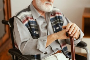 Tekerlekli sandalyede oturan ve baston tutan yalnız yaşlı adam