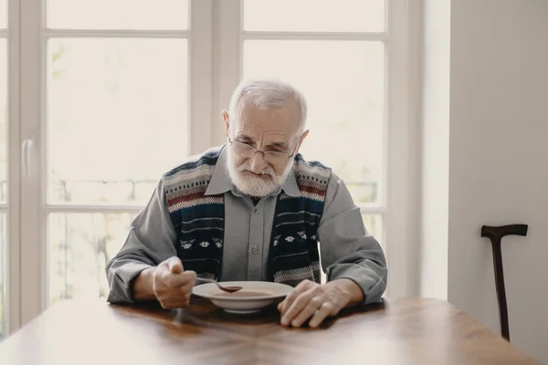 Smutný osamělý starší muž pojídáním polévky v prázdném bytě — Stock fotografie