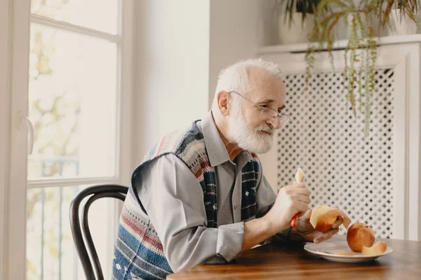 Solitario uomo anziano mangiare una mela al tavolo in casa vuota — Foto Stock