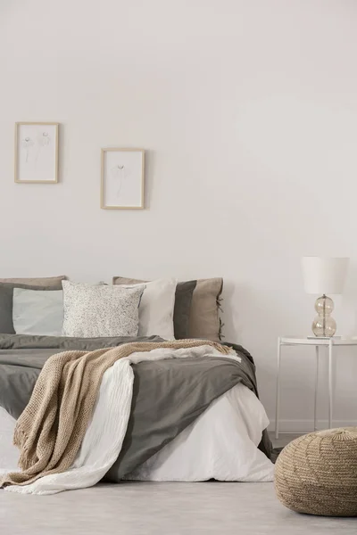 时尚白灯，放在简单的床架上，旁边是温暖的床，配有舒适的灰色床上用品 — 图库照片