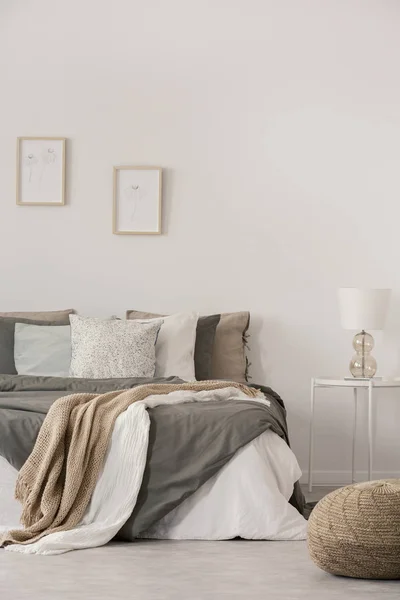 Stylish white lamp on simple nightstand table next to warm bed with cozy grey bedding — Stock Photo, Image