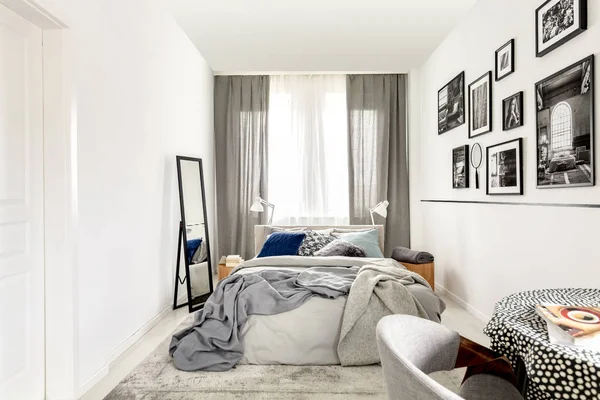 Small bedroom interior with king size, mirror, and black and white photos on the wall — Stock Photo, Image