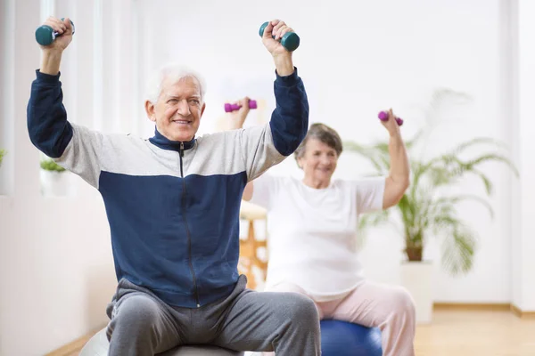 Hombre y mujer mayores haciendo ejercicio en las bolas de gimnasia durante la sesión de fisioterapia en el hospital —  Fotos de Stock
