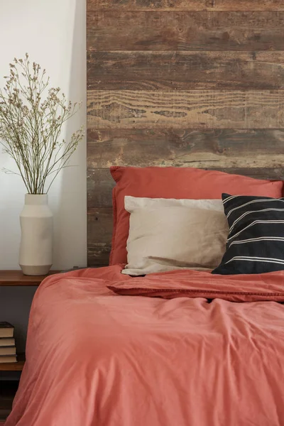 Close-up van een rustiek bed met houten bedkop en rood beddengoed in een lichte slaapkamer interieur. Echte foto — Stockfoto