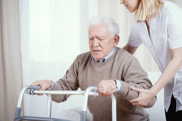 Oudere grijze man met walker en jonge verpleegster ondersteunen hem — Stockfoto