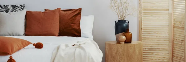 Florero en una mesa de madera junto a una cama en el interior de un dormitorio —  Fotos de Stock