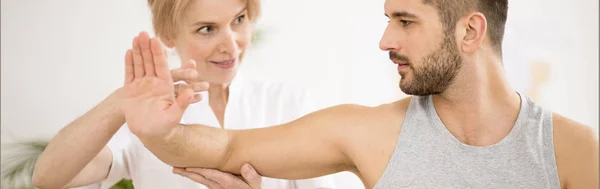 Panoramic view of handsome young man during physiotherapy session with professional doctor — Stock Photo, Image