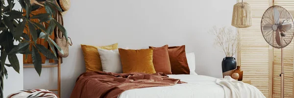 Real photo of a cozy bedroom interior with colorful pillows, fan and close-up of a plant — Stock Photo, Image