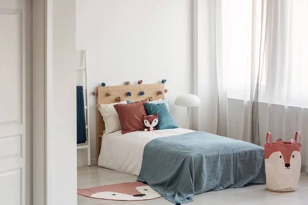Jasne wnętrze sypialni z pojedynczym łóżkiem z turkusowym kocem na białej pościeli i kolorowymi poduszkami i zabawką — Zdjęcie stockowe