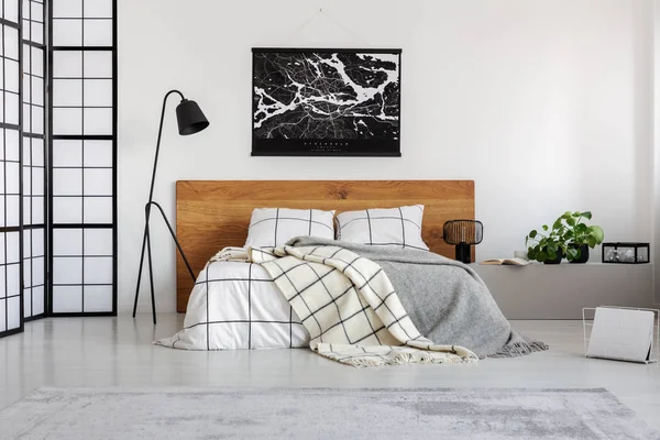 Zwarte kaart op witte muur boven houten hoofdeinde in eenvoudige slaapkamer interieur — Stockfoto