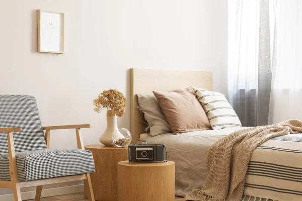 Vintage camera on round wooden table in the middle of elegant bedroom with retro armchair and single bed with beige bedding and flowers in vase — Stock Photo, Image