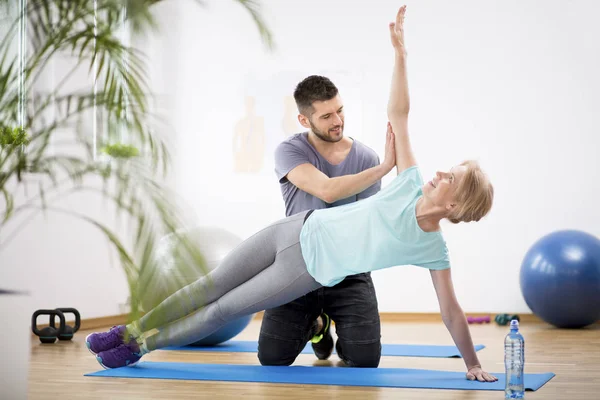 Mulher de meia idade se exercitando no tapete azul durante a fisioterapia com jovem médico do sexo masculino — Fotografia de Stock