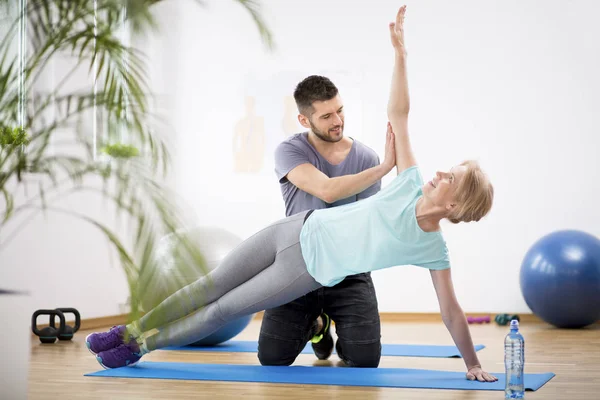 Middle age woman exercising on blue mat during physiotherapy with young male doctor — Stock Photo, Image